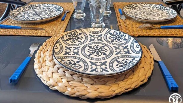 A dining table set with patterned plates, glasses, and cutlery, surrounded by chairs. - L'Arcolan - VALRAS PLAGE (VALRAS PLAGE)