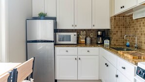A compact kitchen with white cabinets, a stainless steel refrigerator, a microwave, a coffee maker, and a sink with a faucet. - Stylish UM Loft on Diag (Ann Arbor)