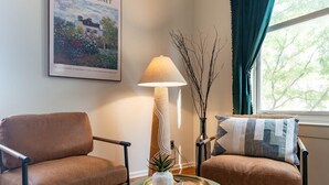 A living room with two brown leather sofas, a green ottoman, a floor lamp, a vase with branches, and a framed picture on the wall. - Stylish UM Loft on Diag (Ann Arbor)