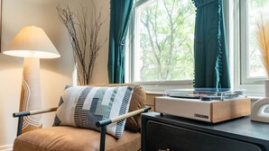 A cozy room with a brown leather chair, a patterned cushion, a table with a turntable, and a lamp. - Stylish UM Loft on Diag (Ann Arbor)