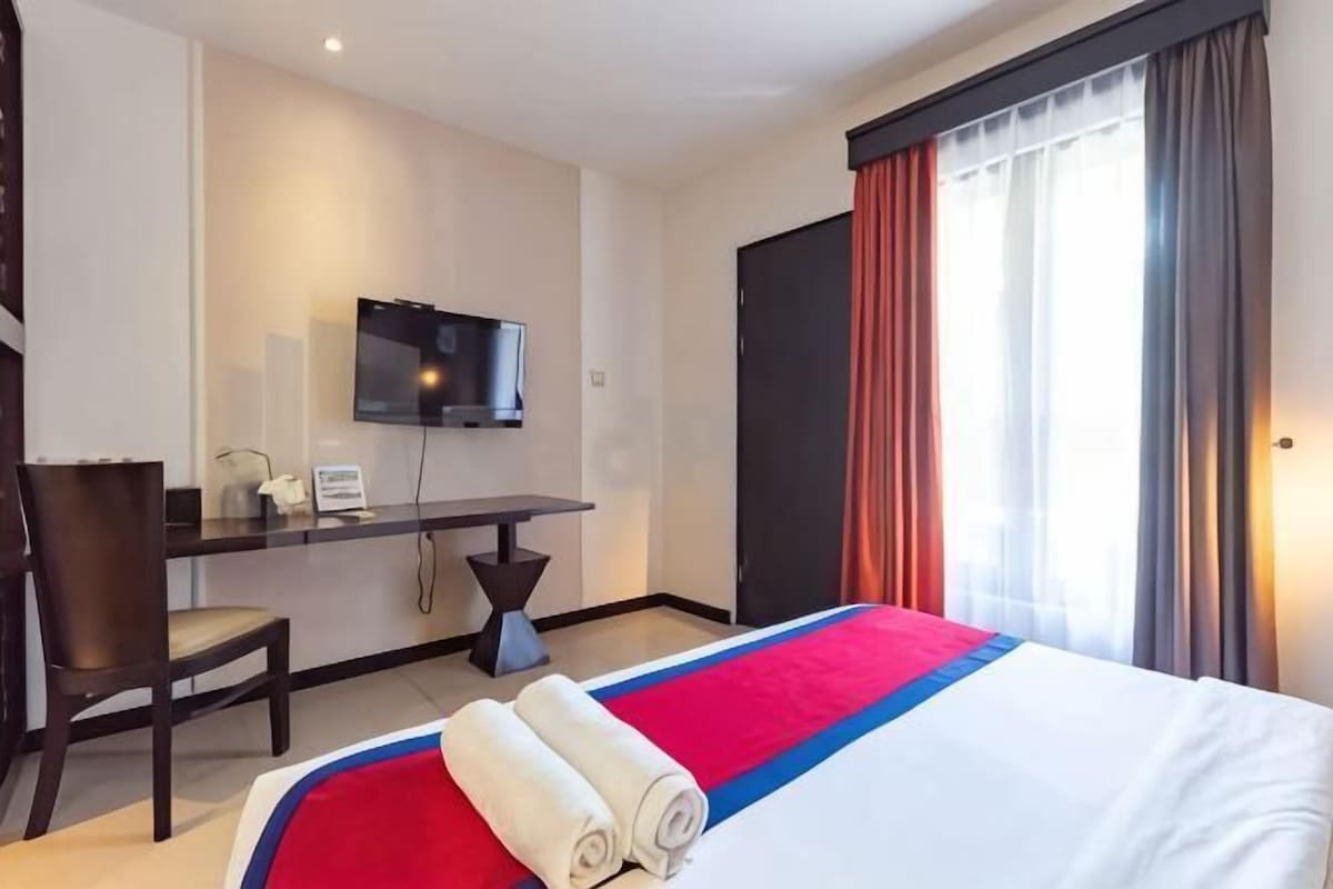 Une chambre d’hôtel équipée d’un lit, d’un bureau, d’une chaise, d’une télévision et d’une fenêtre avec des rideaux.