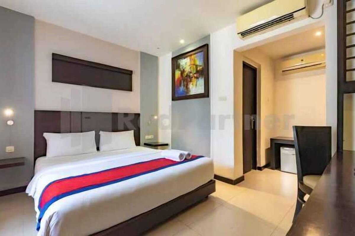 A hotel room with a bed, a desk, and an air conditioning unit.