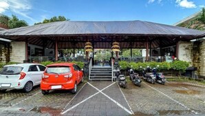 A covered parking area with cars and scooters parked, a staircase leading to a building, and a clear sky. - Ozz Hotel Kuta Bali manage by Ozz Group (Bali)