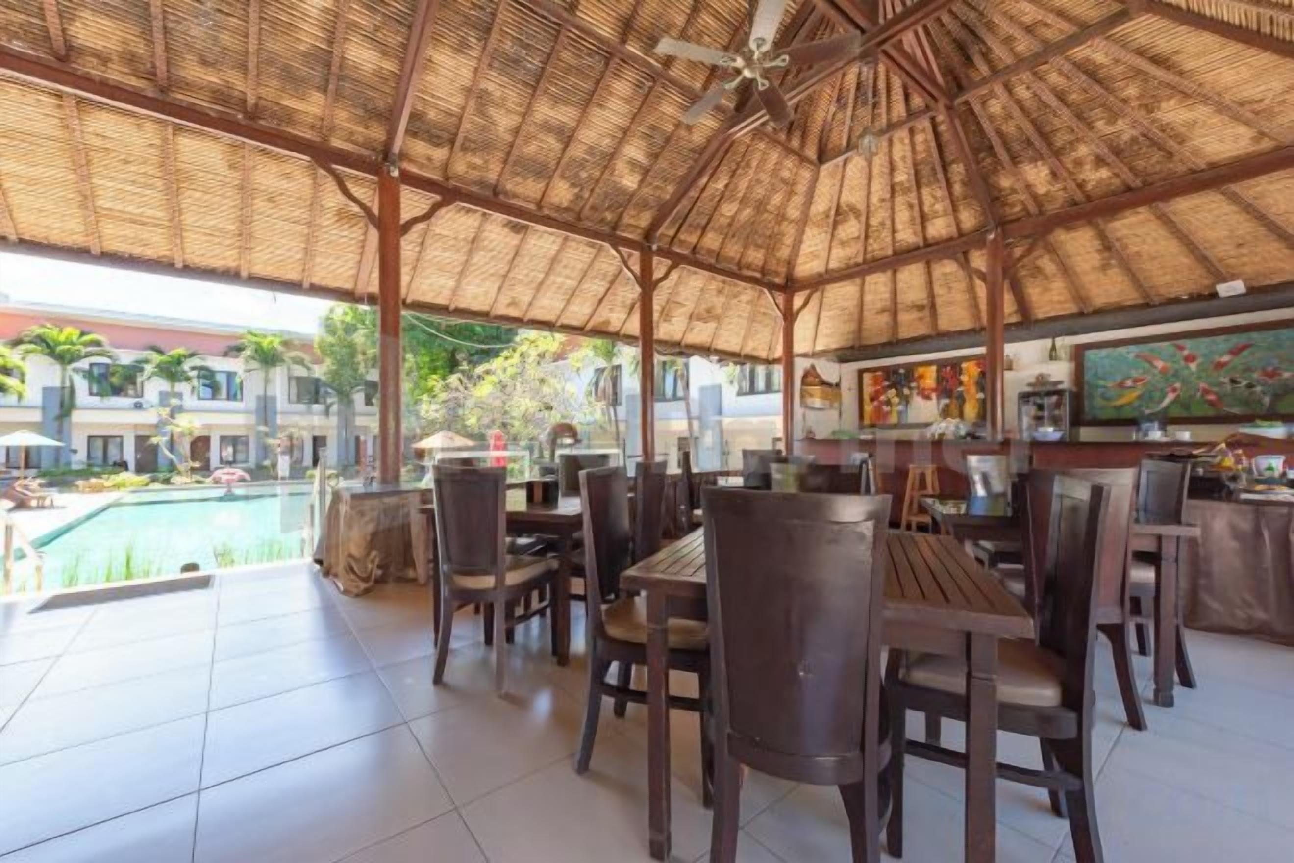An outdoor dining area with a thatched roof, tables, and chairs.