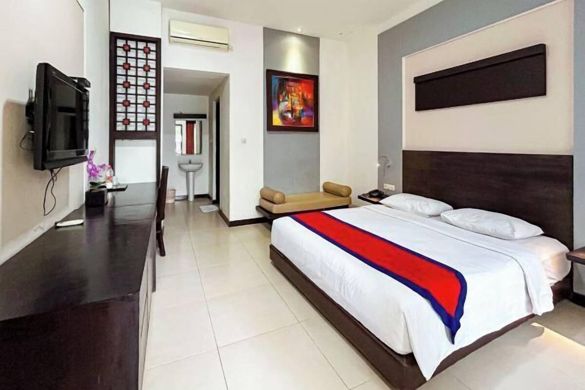 A modern hotel room with a bed, bedside table, TV, and a decorative wall panel.
