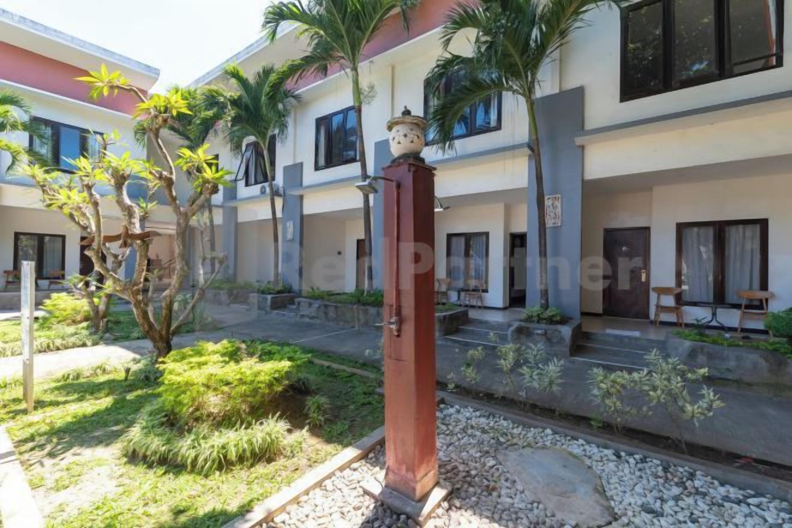 Un cortile con una colonna centrale, palme e un edificio con numerose finestre e porte.