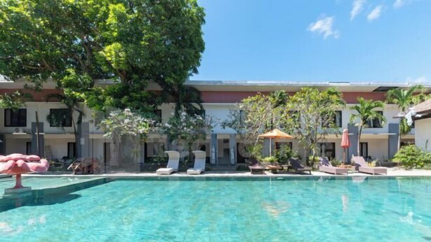 A clear swimming pool with lounge chairs and umbrellas, surrounded by a building with multiple balconies and greenery. - Ozz Hotel Kuta Bali manage by Ozz Group (Bali)