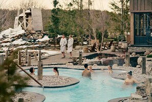 Eine natürliche Thermalquellenlandschaft mit mehreren Pools, Holzbauten und einem Gebäude mit großen Fenstern.