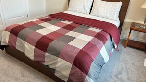A bed with a checkered bedspread, a wooden headboard, and a bedside table with a lamp. - Clean and Spacious 4-bdrm Family home in Whitby! (Whitby)