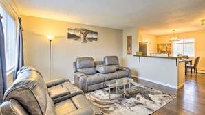 A modern living room with a gray leather sofa, a glass coffee table, and a large rug. There is a dining area with a table and chairs visible in the background. - Charming Columbus Home about 7 Mi to Ohio State! (Columbus)