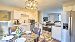 A modern kitchen with white cabinets, stainless steel appliances, and a dining area with a glass table set for four. - Charming Columbus Home about 7 Mi to Ohio State! (Columbus)