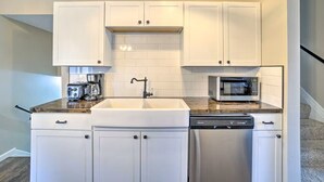 A compact kitchen with white cabinets, a stainless steel dishwasher, a microwave, and a coffee maker. - Charming Columbus Home about 7 Mi to Ohio State! (Columbus)