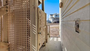 A wooden structure with a slatted design, leading to a house with a visible front porch and a clear sky. - Barracuda: Cozy Buxton Getaway w/ Ocean Views (Buxton)