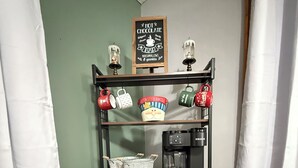 A cozy bar area with a sign reading "HOT CHOCOLATE BAR," shelves with mugs, a coffee machine, and decorative reindeer figures.
