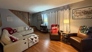 Un salón acogedor con una escalera de madera, un sofá, un sillón y una lámpara.