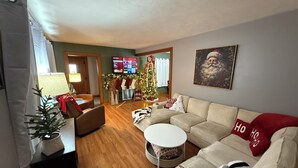 Una sala de estar con sofá, mesa de centro, una mesita auxiliar, chimenea, árbol de Navidad y televisor montado en la pared.