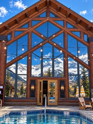 Un chalet en bois doté d’une grande piscine et offrant une vue sur les montagnes.