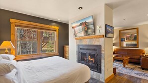 Ein Schlafzimmer mit einem großen Bett, einem Kamin, einem Fenster mit Blick auf Bäume und einem Wohnbereich mit einer Couch und einem Couchtisch.