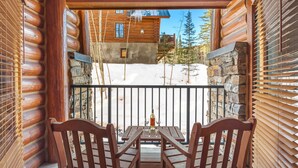 Eine Holzhütte mit steinernen Fundament, einem Balkon mit Tisch und Stühlen und Blick auf eine verschneite Landschaft.