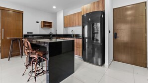 Una cocina moderna con una isla central, refrigerador de acero inoxidable, armarios de madera y una zona con taburetes de bar.