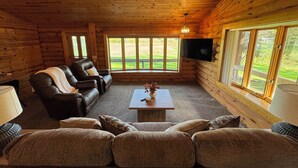A log cabin interior with a leather sofa, a coffee table, and a TV mounted on the wall.