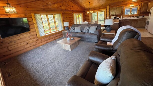 A log cabin interior with a living room, sofa, coffee table, and a kitchen area.