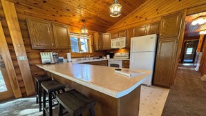 A kitchen with wooden cabinets, a large island with stools, a refrigerator, and a microwave.