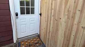 Une porte en bois avec un cadre blanc, un petit porche doté d’un paillasson et une clôture en bois.