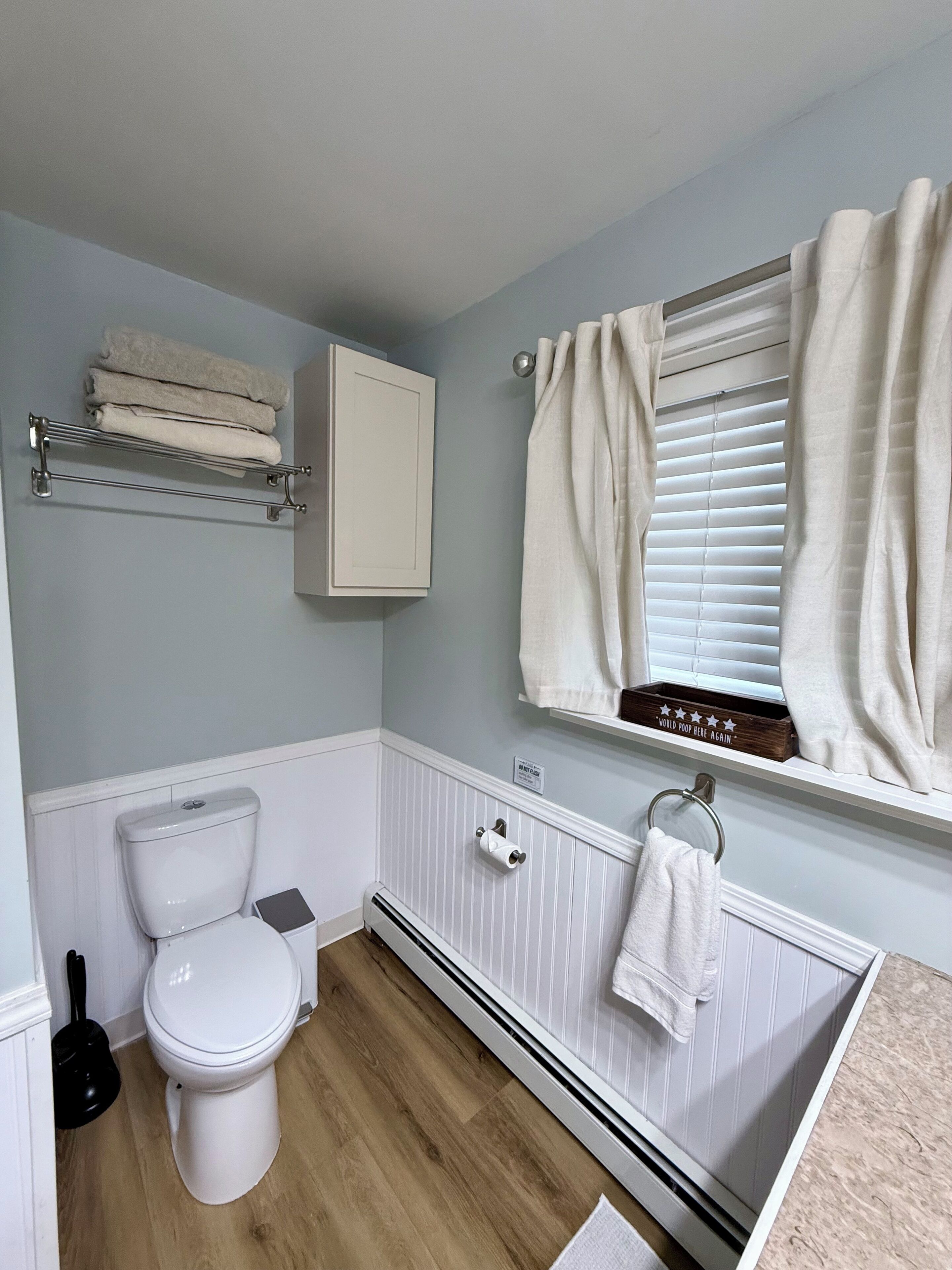 A bathroom with a toilet, a towel rack, a radiator, and a window with curtains.