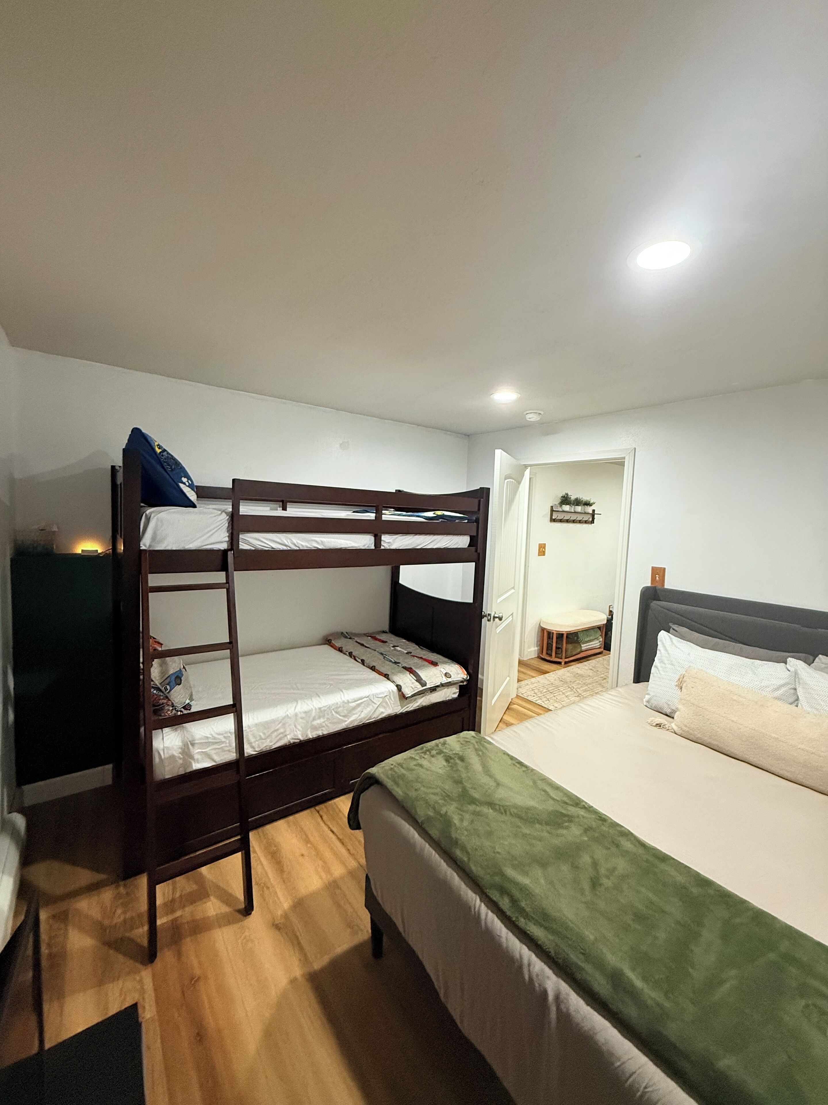 A bunk bed room with a single bed, a door leading to another room, and a small table with a chair.