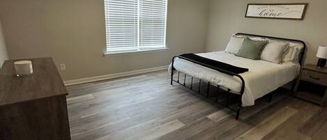 A bedroom with a bed, a nightstand, a desk, and a window with blinds.