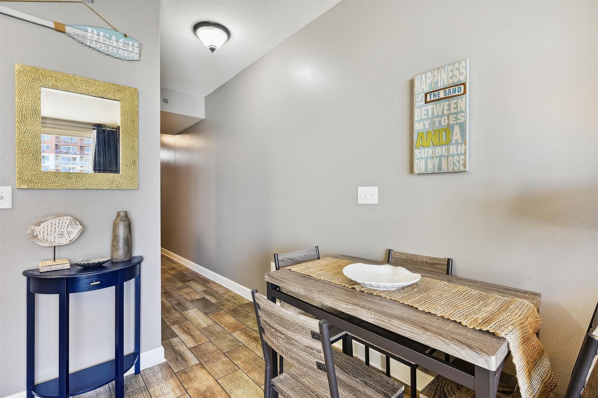 A dining area with a table set for two, a blue console table, and a wall-mounted mirror.