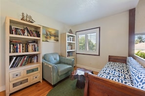 A cozy room with a wooden bed, a green leather chair, and two bookshelves filled with books and decorative items.