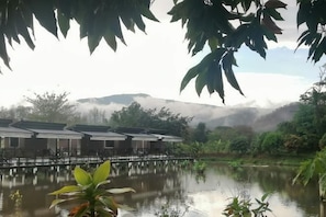 A tranquil lakeside setting with traditional-style buildings, a wooden bridge, and lush greenery. - Monthatip vill (Chom Thong)