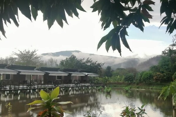 A tranquil lakeside setting with traditional-style buildings, a wooden bridge, and lush greenery. - Monthatip vill (Chom Thong)