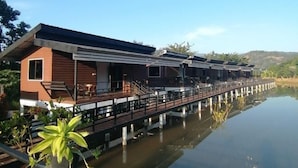 A row of modern, single-story cabins with a wooden exterior and a balcony, connected by a wooden deck over water. - Monthatip vill (Chom Thong)