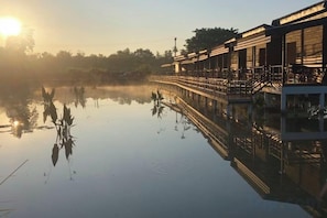 A calm body of water reflecting a building with a bridge, surrounded by trees. - Monthatip vill (Chom Thong)