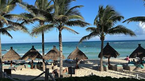Een strand met rieten parasols, ligbedden en palmbomen.