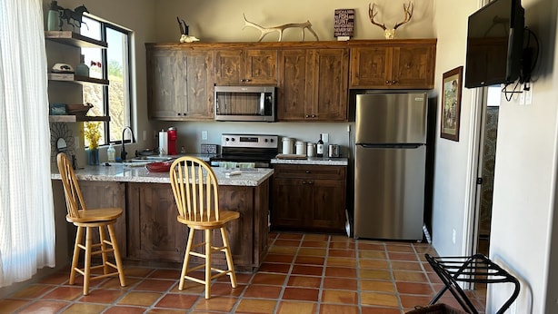A kitchen with wooden cabinets, a stainless steel refrigerator, and a tiled floor.
