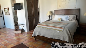 A bedroom with a bed, bedside lamps, a television, a wooden door, and a tiled floor.