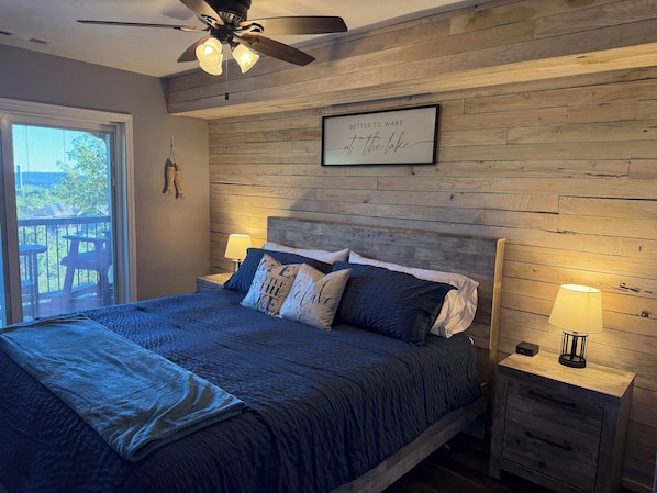 Ein Schlafzimmer mit Holz-Kopfteil, einem Bett mit blauer Bettwäsche, zwei Nachttischlampen und einem Deckenventilator.