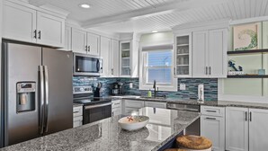 A modern kitchen with white cabinetry, granite countertops, stainless steel appliances, and a central island with stools.