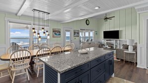 A spacious kitchen with a large island, wooden chairs, and a view of the ocean.