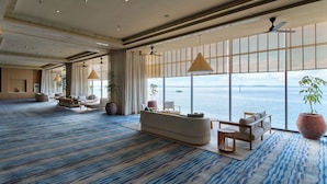 Un hall d’hôtel spacieux, doté d’un grand espace salon, de grandes fenêtres offrant une vue sur la mer et d’un tapis à motifs.