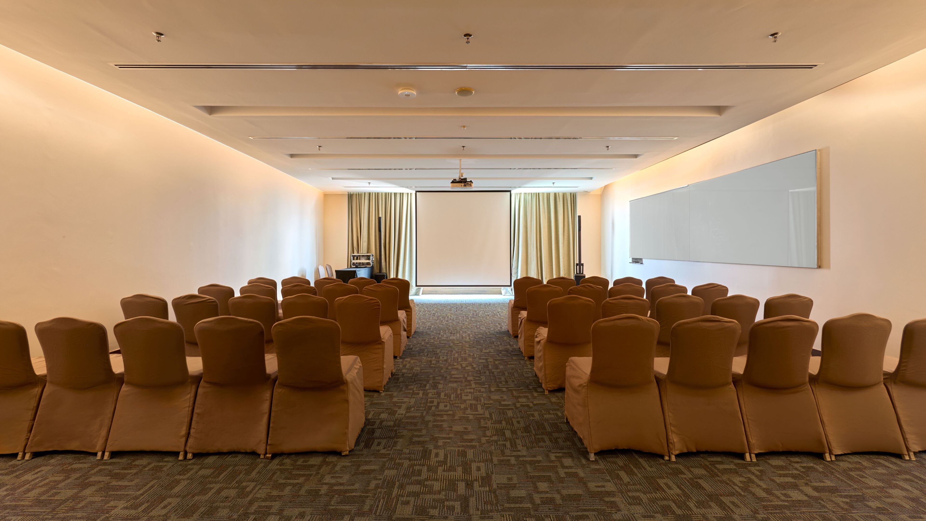 Un salón de conferencias con filas de sillas, una pantalla de proyector y una pizarra.