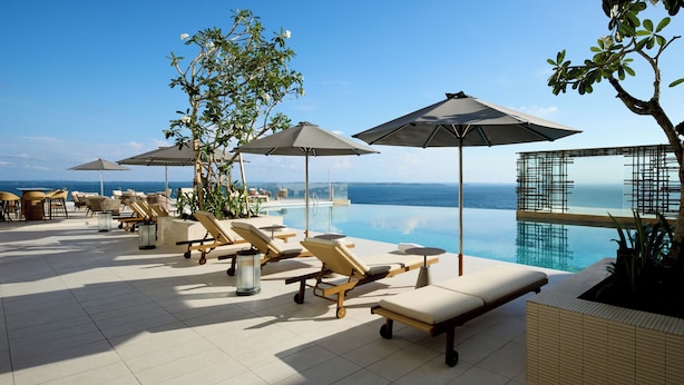 Une piscine à débordement située sur le toit, avec des chaises longues et des parasols, offrant une vue sur la mer.