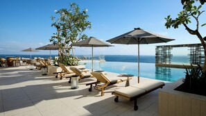 Ein Infinity-Pool auf dem Dach mit Liegestühlen und Sonnenschirmen, mit Blick auf das Meer.