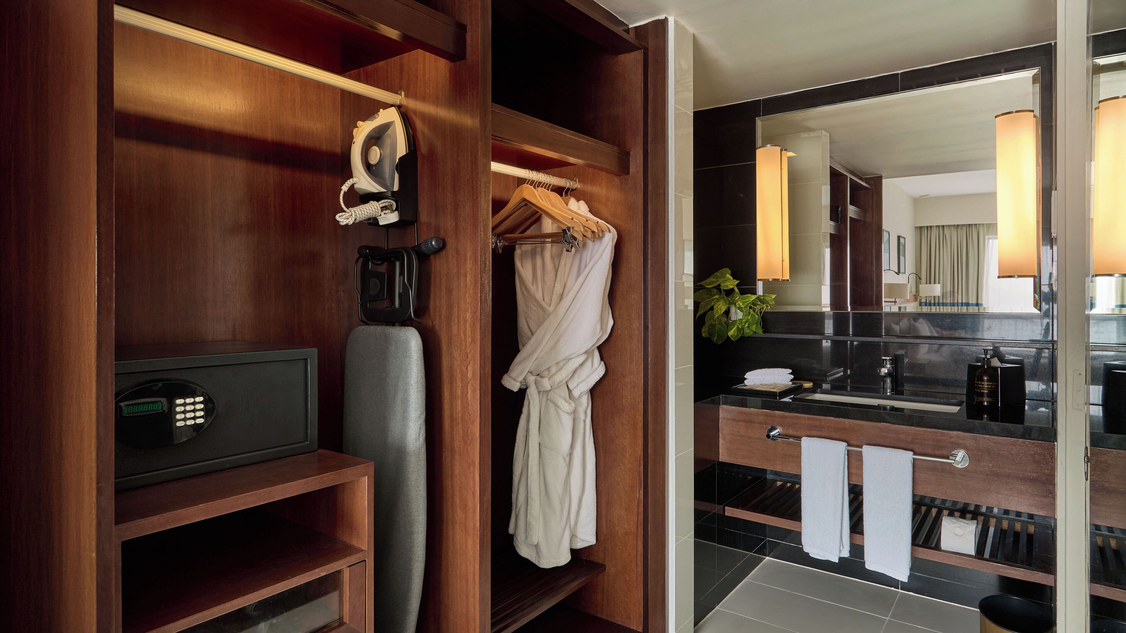 A hotel bathroom with a wooden vanity, a mirror, a towel rack, and a robe hanging on a hook.