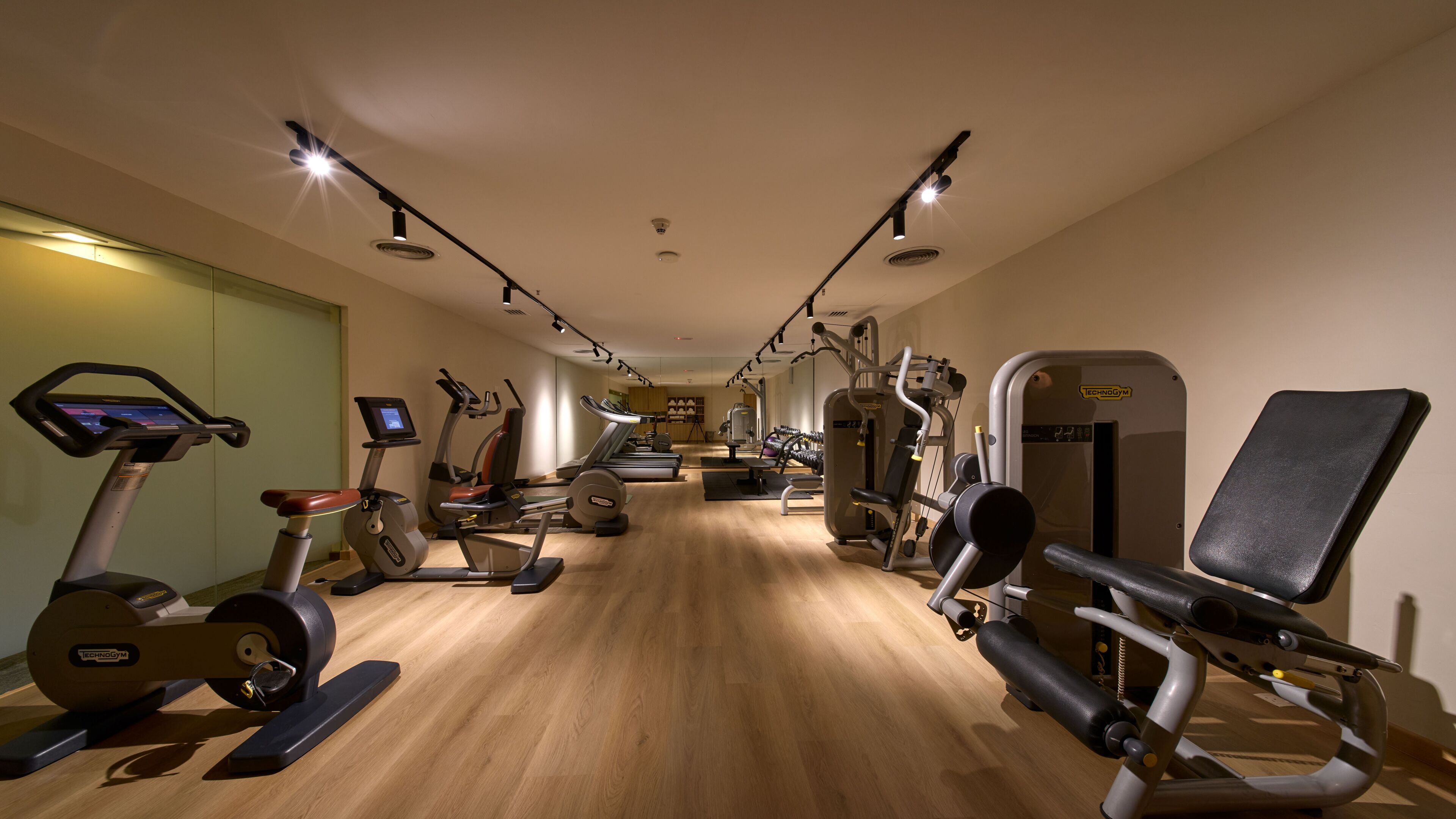 A gym with cardio machines, weightlifting equipment, and a mirror wall.