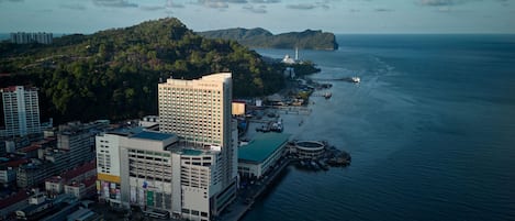 A coastal cityscape with a prominent hotel named 'ORION' featuring a modern design, waterfront access, and a view of the sea.